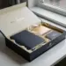 Geöffnete Onboarding-Box mit Notizbuch, Seidenpapier und Willkommenskarte in Navy, Creme und Gold auf modernem Schreibtisch.
