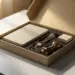 Geöffnete Onboarding-Box aus mattem Karton mit Notizbuch, Lanyard und kleinem Willkommensgeschenk auf weißem Schreibtisch, warmes goldenes Licht.