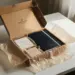 Geöffnete Onboarding-Box mit Notizbuch, Willkommensmaterialien und Firmengeschenk auf weißem Schreibtisch, weiches Seitenlicht.