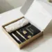 Leicht geöffnete Premium-Onboarding-Box auf weißem Schreibtisch mit Willkommensmaterialien, Seidenpapier und gebrandeten Artikeln in Gold und Anthrazit.