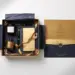 Aufgeklappte Onboarding-Box mit Marken-Seidenpapier, Welcome-Artikeln und versiegeltem Umschlag auf weißer Fläche in Navy und Gold.