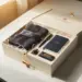 Geöffnete Onboarding-Willkommensbox mit gebrandetem Merchandise und Seidenpapier auf weißem Schreibtisch, warmes Fensterlicht.