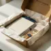 Geöffnete Premium-Onboarding-Willkommensbox mit Notizbuch, Stift und kleinen Geschenken in Seidenpapier auf weißem Schreibtisch.