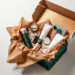Geöffnete Premium-PR-Box in dunkelgrün mit Kupferfolie zeigt Lifestyle-Produkte in cremefarbenen Schaumstoffeinsätzen