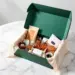 Offene Premium-PR-Box in Waldgrün mit Roségold-Akzenten zeigt Skincare-Flaschen, Kaffee und Accessoires auf Marmortisch