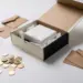 Geöffnete Premium-Geschenkbox mit strukturiertem Seidenpapier, umgeben von Münzen und Kraftpapier-Umschlägen auf weißem Untergrund.