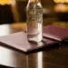 Geöffnete Speisekarte in burgunderrotem Leder auf Restauranttisch, darauf eine beschlagene Glasflasche Softdrink im warmen Ambiente.