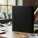 Schwarzer Versicherungsordner auf Designerschreibtisch mit Farbmustern, Hand greift nach Ordner, natürliches Licht
