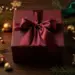 Luxuriöse Weihnachts-Geschenkbox mit burgunderroter Schleife, Tannenzweigen und goldenen Kugeln auf dunklem Walnussholz.