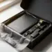 Geöffnete matte schwarze Onboarding-Geschenkbox mit Notizbuch, Lanyard und Accessoires auf weißem Schreibtisch, goldene Akzente, natürliches Fensterlicht.