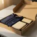 Geöffnete Onboarding-Box mit Firmen-Hoodie, Notizbuch, Stift und Willkommenskarte auf weißem Schreibtisch im warmen Licht.