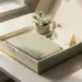 Geöffnete Premium-Onboarding-Box mit Notizbuch, kleiner Pflanze und Willkommenskarte in cremefarbenen und salbeigrünen Tönen mit Goldakzenten.