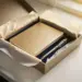 Aufgeklappte Onboarding-Geschenkbox mit Notizbuch, Stift und Seidenpapier auf weißem Schreibtisch in warmem Licht.
