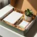 Geöffnete Onboarding-Geschenkbox mit Notizbuch, Stift, Sukkulente und Willkommenskarte auf weißem Schreibtisch.