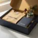 Geöffnete Onboarding-Willkommensbox mit gefältetem T-Shirt, Notizbuch, kleiner Sukkulente und Zweig auf weißer Oberfläche.