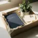 Geöffnete Onboarding-Geschenkbox mit Notizbuch, Stift, kleiner Pflanze und Willkommenskarte in Navy, Creme und Gold auf weißem Schreibtisch.